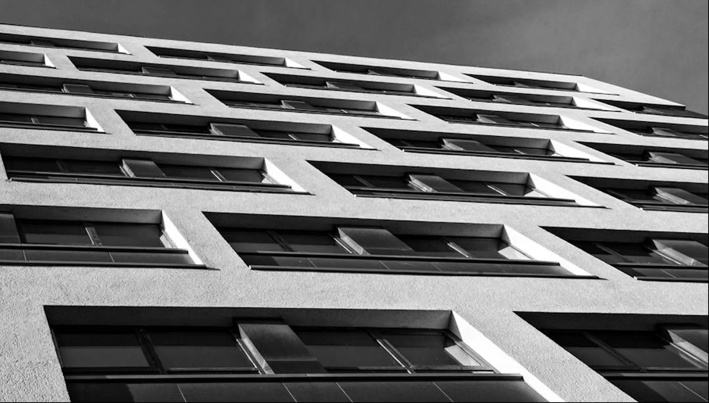 Low-angle view of the facade: rows of dark-framed windows in horizontal bands across a white surface; black and white.