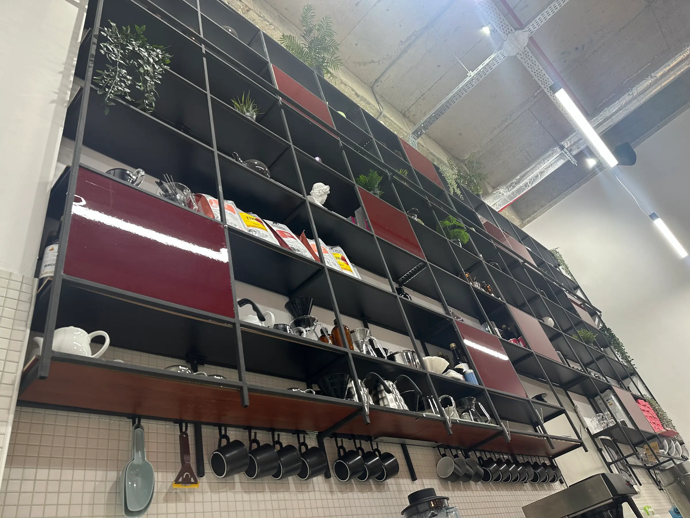 Alttan bakış: siyah metal raflar, bordo paneller ve asılı kupalar.