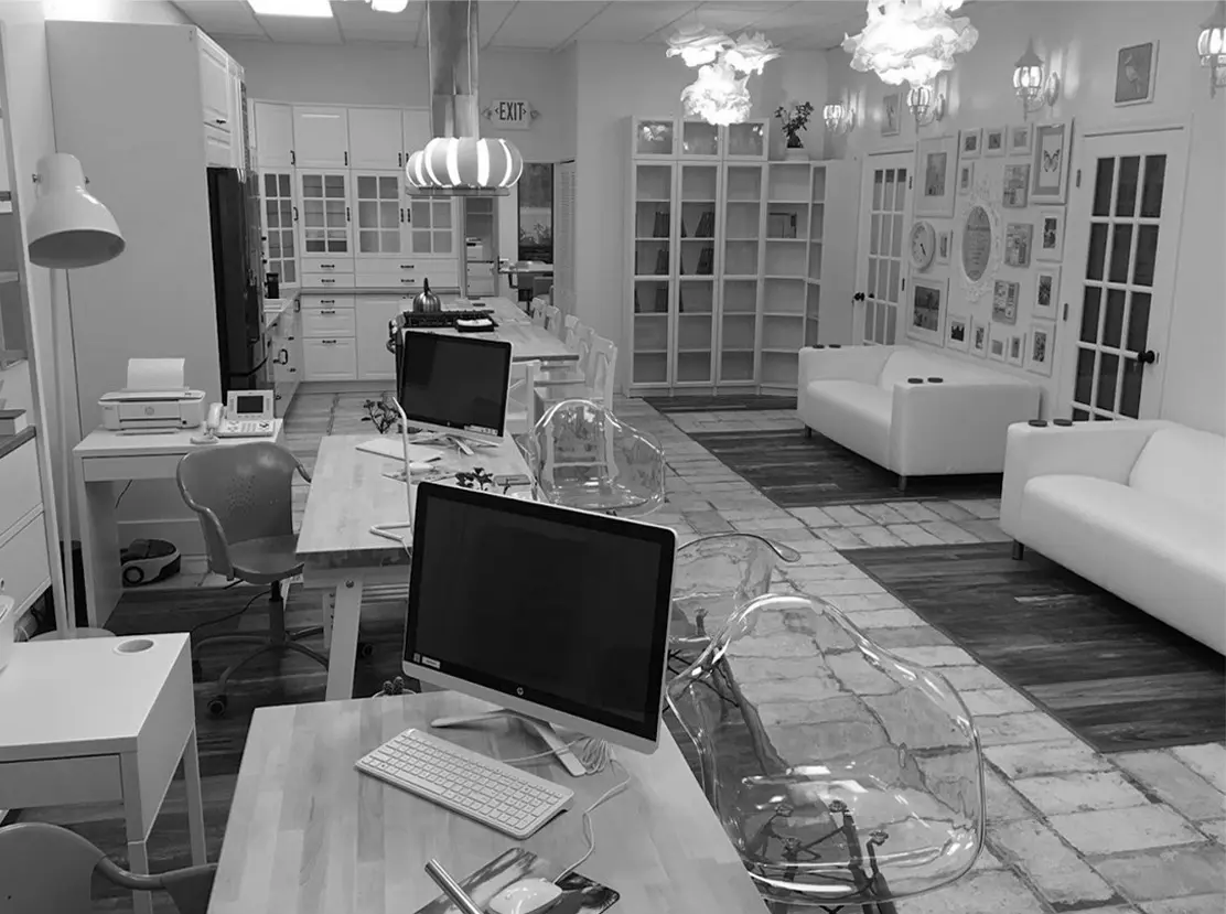 Ofis bölümü: masalar ve ekranlarla çalışma alanı; siyah-beyaz.