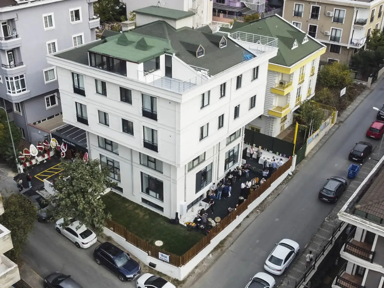 Aerial view of the white building with its green roof, the garden hosting an opening event and the surrounding street.
