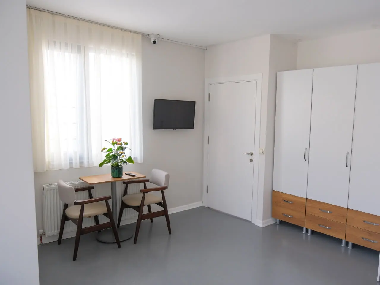 Room with a table and two chairs by the window and a white wardrobe.