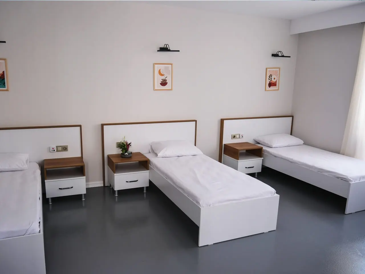 Symmetrical three-bed room with wall lights and pictures above the beds.
