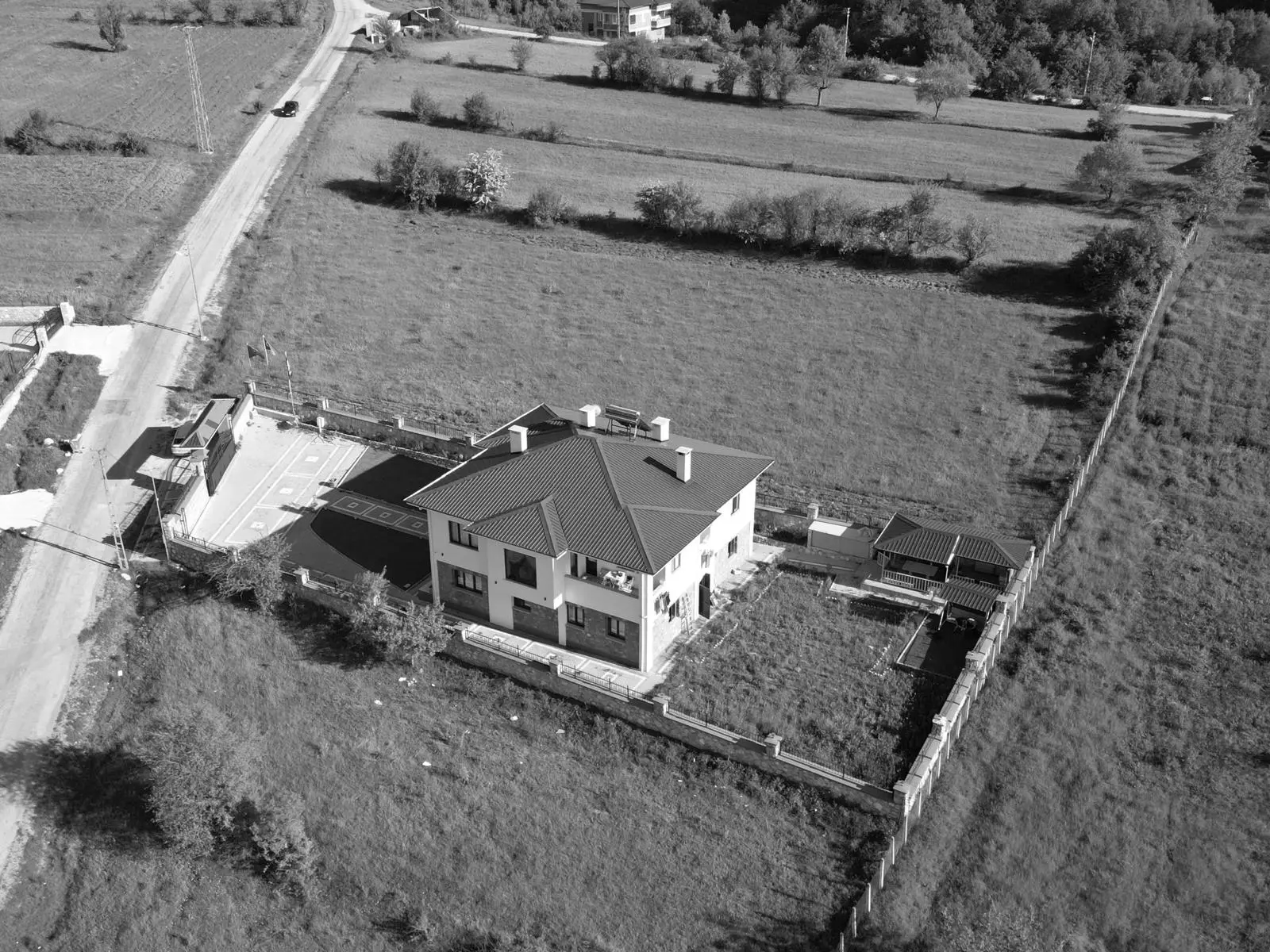 Dron görüntüsü: yeşil arazide ev, bahçe ve çevredeki tarlalar.